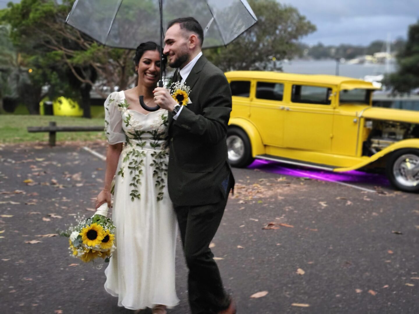 A joyful couple celebrating their wedding day, posing elegantly beside our yellow hot rod, the ideal wedding car for hire